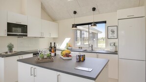 Une cuisine moderne avec des meubles blancs, un îlot central, un four à micro-ondes, un réfrigérateur et une fenêtre donnant sur une maison.