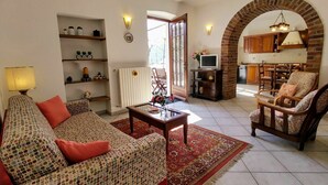 Un soggiorno con divano, poltrone, tavolino e televisione. Si intravede una cucina attraverso un arco.