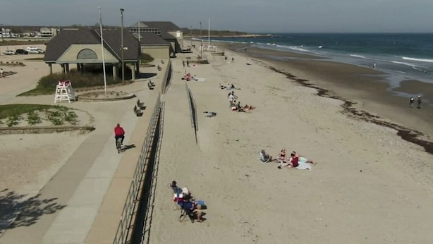 A beach with a walkway, beachgoers, and a building in the background.
