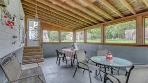 A covered patio with a wooden ceiling, a round glass table, and chairs.