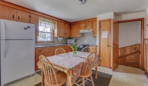 Enjoy meals at the dining table with four chairs, surrounded by a vase with flowers and a window with a lace curtain.