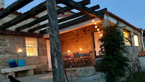 A stone building with a covered patio, outdoor seating, and a table set for dining. - Casa de Ventozella (Penafiel)