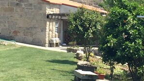 A stone building with a tiled roof, a small balcony, and a garden with potted plants and a lawn. - Casa de Ventozella (Penafiel)