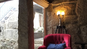 A red armchair with a blue pillow in a stone-walled room with a staircase visible through a glass door. - Casa de Ventozella (Penafiel)