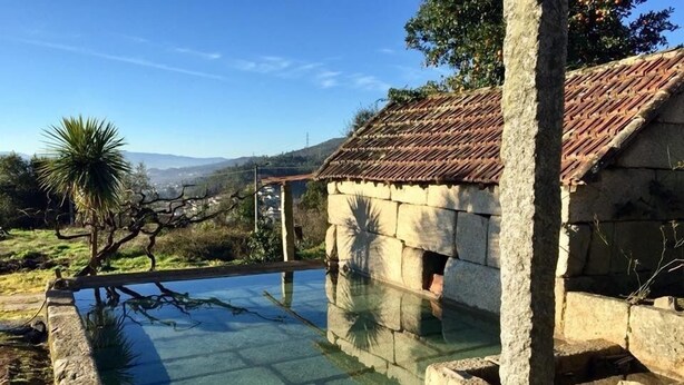 A stone pool with clear water, surrounded by stone walls and a tiled roof structure. - Casa de Ventozella (Penafiel)