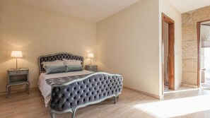 A bedroom with a tufted headboard bed, two bedside tables with lamps, and a door leading to a stone wall.