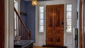 A wooden front door with a glass panel, a wooden staircase with a handrail, and a wall-mounted light fixture. - Waterfront, Swimming Hotspot, Private Down Town Location, Farmhouse (Waitsfield)