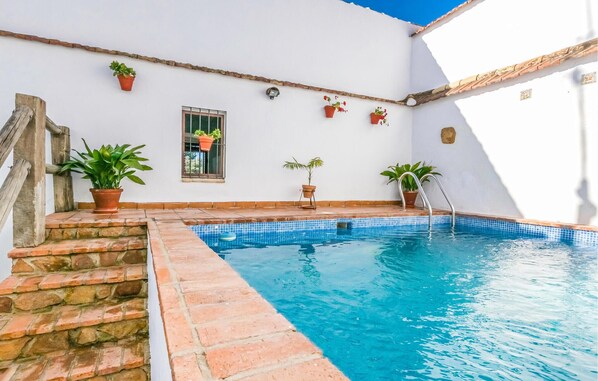 A small, private swimming pool with steps leading into it, surrounded by white walls and potted plants.