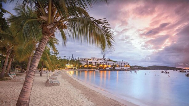 Ein Strandhotel mit Pool, Palmen und Blick auf den Sonnenuntergang.