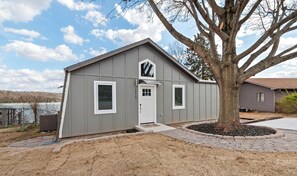 A small, single-story building with a gray exterior, a white door, and two windows.