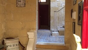 Eine Treppe führt zu einem Raum mit einem gemusterten Boden, einer Wanduhr und einem Stuhl mit einem gemusterten Kissen.
