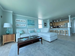 A living room with a white sofa, a coffee table, and a kitchen area in the background.
