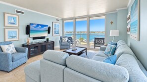 A living room with a large TV, a sofa, a chair, and a coffee table. - Sabine 4D Waterfront Condo Sleeps 6, Corner Unit - Pool (Pensacola Beach)