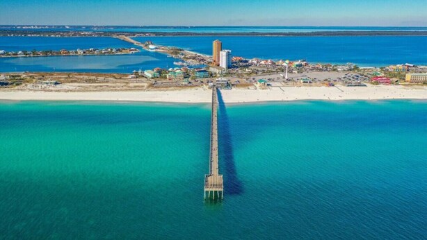 Luchtbeeld van een kustgebied met een opvallende pier die zich uitstrekt in het turquoise water.
