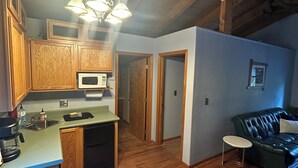 Una cocina con armarios de madera, microondas y cafetera. Hay una mesa de comedor con sillas en el centro de la habitación.