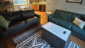 Una sala de estar acogedora con chimenea, dos sofás de cuero, un tapete estampado y una cocina al fondo.
