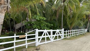 A white wooden fence with a sign that reads "Bottles 4 AGUA" along a sandy path with palm trees and greenery in the background. - Amazing right on the water, BEACHFRONT studio near Tamarindo (POTRERO)
