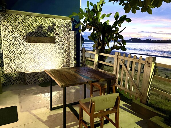 A patio with a wooden table and chairs, a patterned wall, and a view of the sea. - Amazing right on the water, BEACHFRONT studio near Tamarindo (POTRERO)