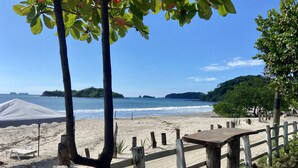 A beach with a wooden fence, a covered area, and a view of the ocean and distant islands. - Amazing right on the water, BEACHFRONT studio near Tamarindo (POTRERO)
