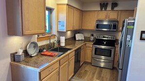 A kitchen with wooden cabinets, a stainless steel refrigerator, a microwave, an oven, and a sink with a towel holder. - Perfect Location! - EV charger, downtown, shuttle, + private hot tub & garage! (Winter Park)