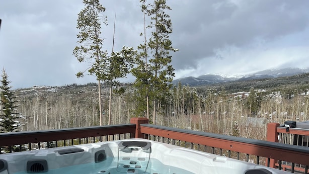 A hot tub on a deck with a view of snow-covered mountains and trees. - Perfect Location! - EV charger, downtown, shuttle, + private hot tub & garage! (Winter Park)