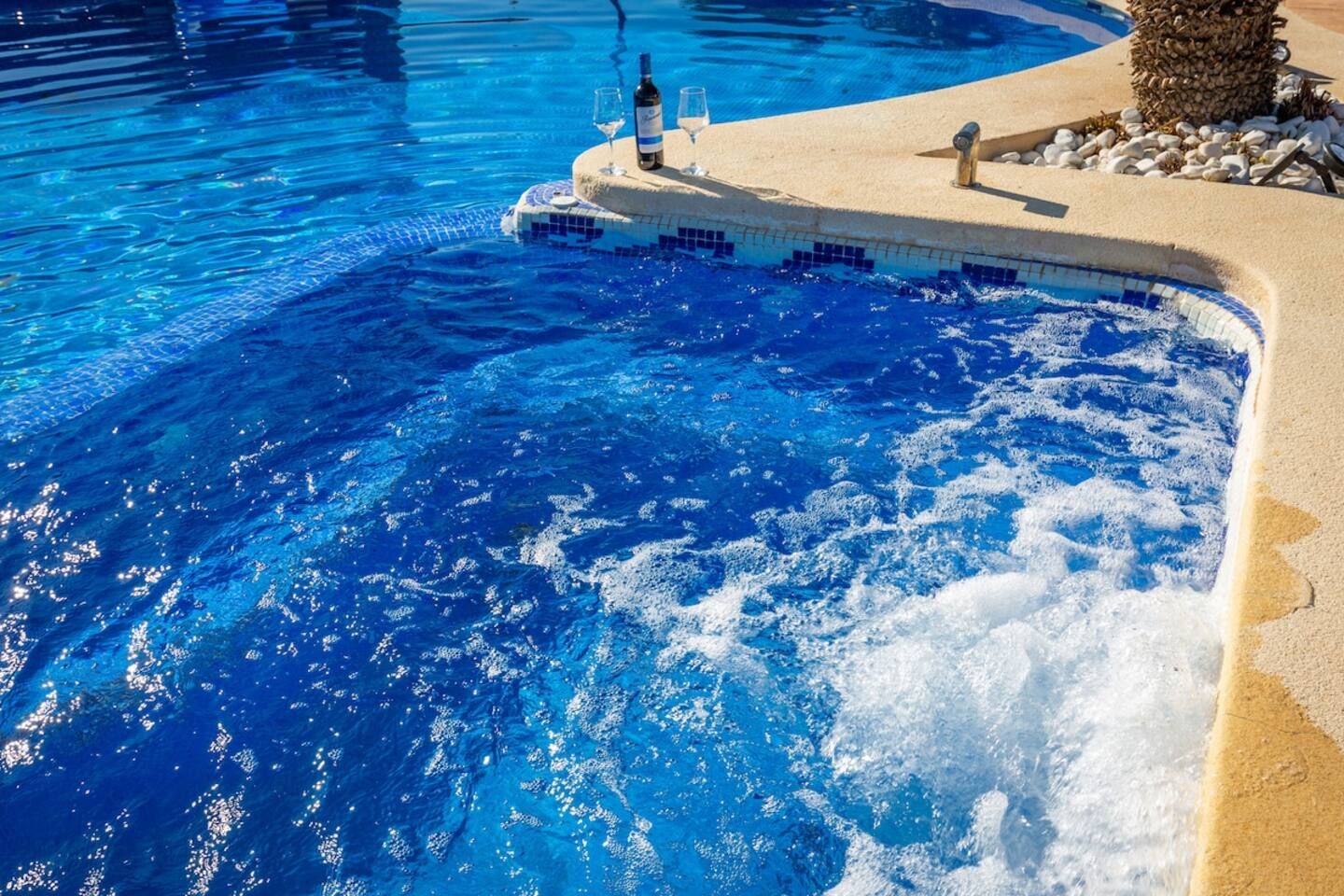 Una piscina con agua azul cristalina, una pequeña isla con una botella y un vaso, y una palmera.