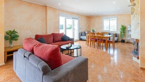 Een ruime woonkamer met een bank, eettafel, stoelen en een open haard.