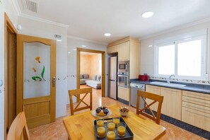 A modern kitchen with wooden cabinets, a dining table with chairs, and a breakfast tray with muffins and orange juice.