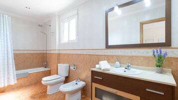 Une salle de bain avec une baignoire, deux toilettes, un bidet, un lavabo avec un miroir et une plante en pot.