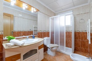 Casa de banho com lavatório, espelho, sanita e chuveiro.