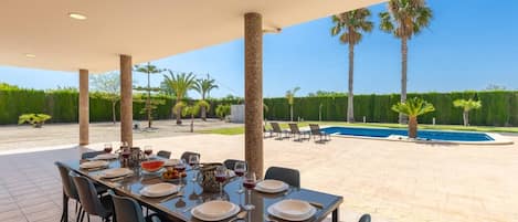 An outdoor dining area with a pool and palm trees in the background.