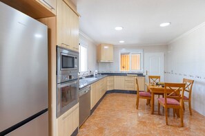A modern kitchen with stainless steel appliances, wooden cabinets, and a dining area with a table and chairs. - Fidalsa Dom Perignon (Crevillente)
