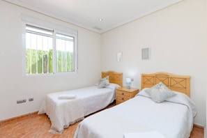 Une chambre avec deux lits simples, une table de chevet, une fenêtre donnant sur un espace verdoyant et un interrupteur sur le mur.