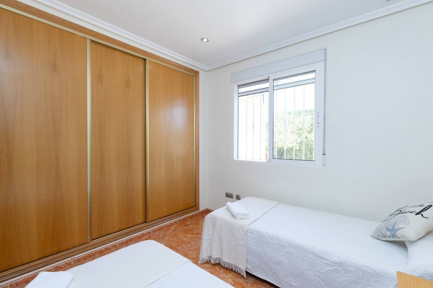 Une chambre avec un lit simple, une armoire en bois, une fenêtre avec des stores et une petite table de chevet.