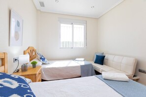 A hotel room with two beds, a sofa, a small table, and a window.
