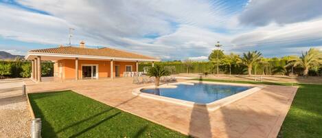 Ein Wohnhaus mit Swimmingpool, überdachter Terrasse und gepflegtem Rasen.