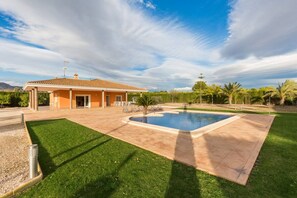 A residential property with a swimming pool, a covered patio, and a well-maintained lawn.