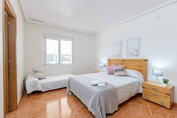 A bedroom with two beds, a wooden headboard, bedside tables with lamps, and a window with blinds. - Fidalsa Dom Perignon (Crevillente)