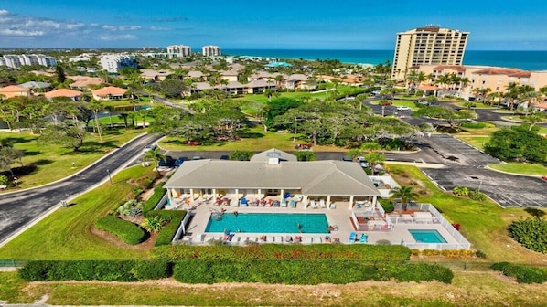 A hotel with a swimming pool, surrounded by greenery and a view of the ocean.