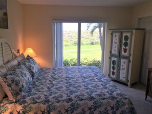 Quarto com cama, mesa de cabeceira, luminária, porta de vidro deslizante para um jardim e um armário com objetos decorativos.