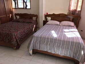 Two wooden beds with patterned bedspreads, a tiled floor, and a window with curtains. - Vacation rental house (Arrondissement de Jacmel)