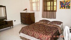 A bedroom with a large bed, a dresser, a mirror, and a window with curtains. - Vacation rental house (Arrondissement de Jacmel)
