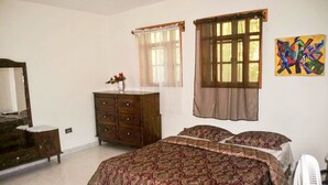 A bedroom with a large bed, a dresser, a mirror, and a window with curtains. - Vacation rental house (Arrondissement de Jacmel)