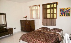 Un dormitori amb un llit gran, un aparador, un mirall i una finestra amb cortines.
