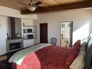 A bedroom with a bed, a fireplace, a ceiling fan, and a door leading to a bathroom.
