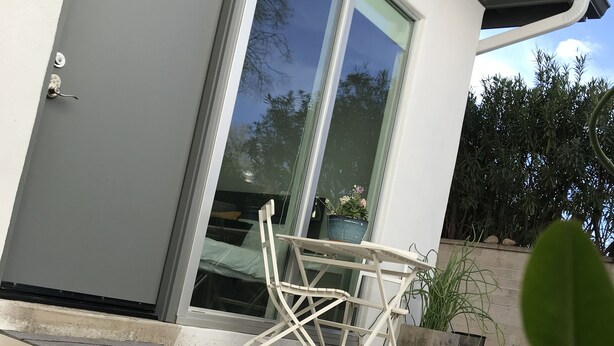 Ein modernes Haus mit einer Schiebetür aus Glas, einem weißen Tisch im Freien und Topfpflanzen.