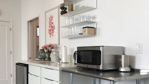 Eine moderne Küche mit Edelstahl-Kühlschrank, Mikrowelle und Kaffeemaschine auf der Arbeitsplatte. Darüber befinden sich Glastrennwände mit verschiedenen Gegenständen.
