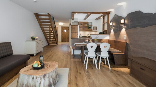 Ein modernes Wohnzimmer mit einer Holztreppe, einem Essbereich mit weißen Stühlen und einer Küche mit Holzschränken.