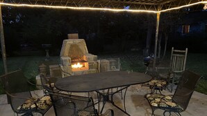 Une terrasse extérieure avec un foyer en pierre, des chaises en métal et une table.