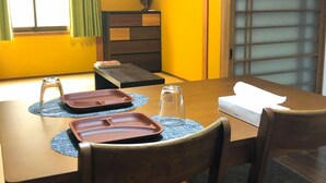 Uma área de refeições com uma mesa de madeira, duas cadeiras, um abajur e uma janela com cortinas.